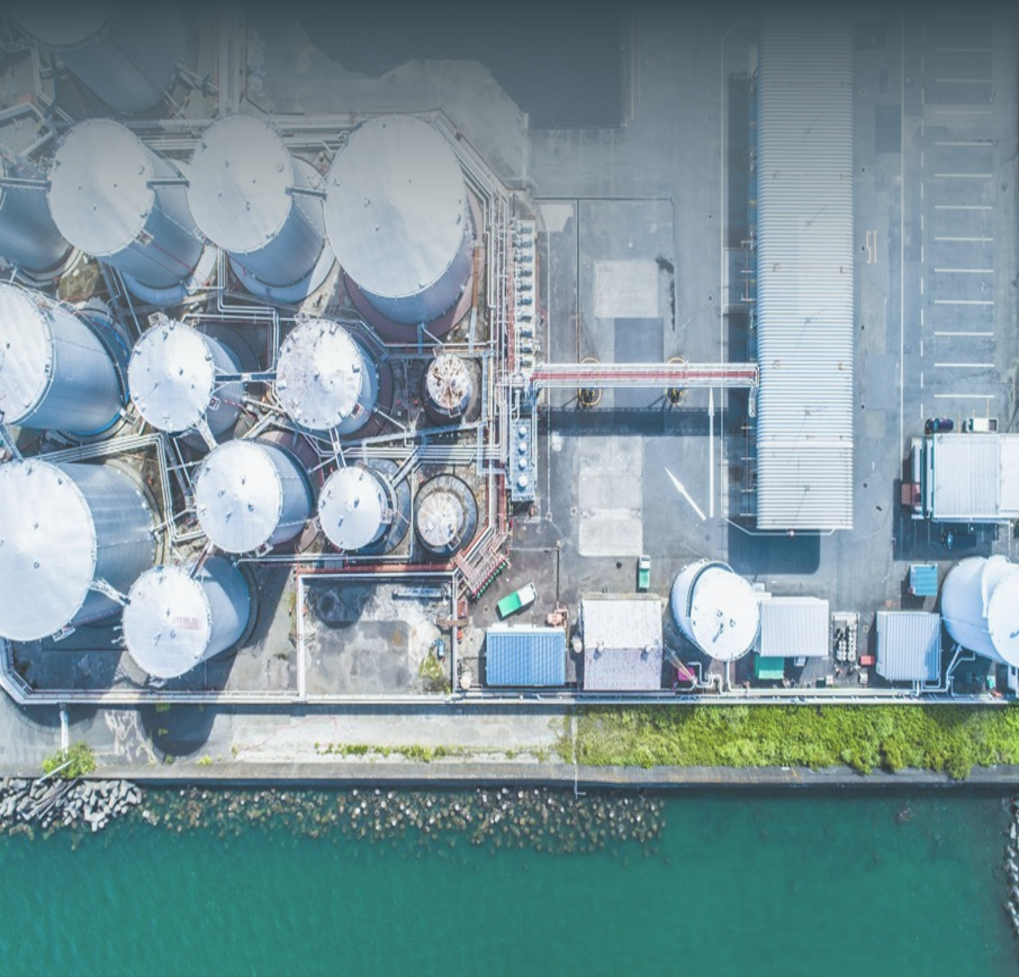 Oil refinery with tall chimneys emitting steam under a clear sky. The facility is surrounded by industrial equipment and pipelines. Visible text: Energy. The environment is modern and industrious, conveying a sense of progress and reliability.